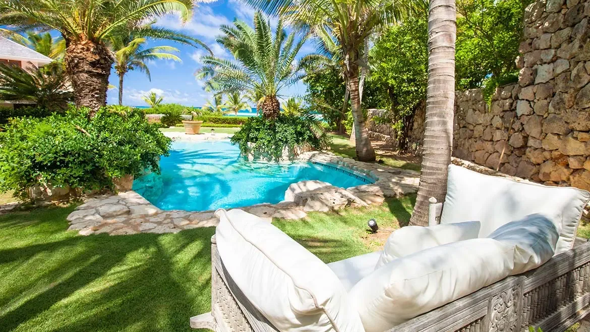 Luxury swimming pool with lounge chairs overlooking tropical green hills and blue ocean.