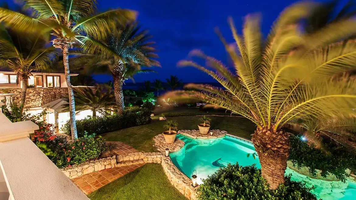 White tiled patio with black dining set, architectural columns, and a blue pool against a red accent wall.