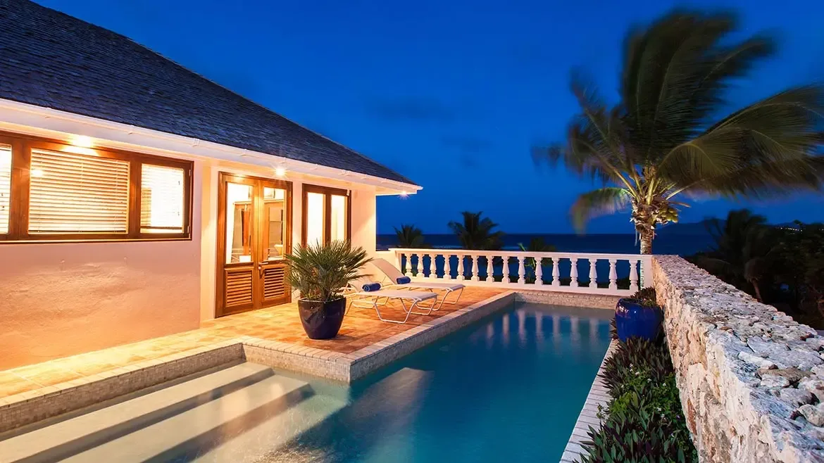 White villa terrace with potted plants, a black dining table, and a scenic view of the ocean and mountains.
