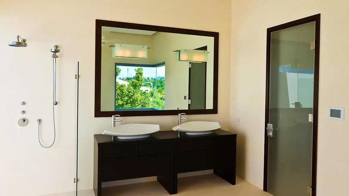 Bathroom vanity with gray mosaic stone countertop, large mirror, and chrome shelving unit with rolled white towels.