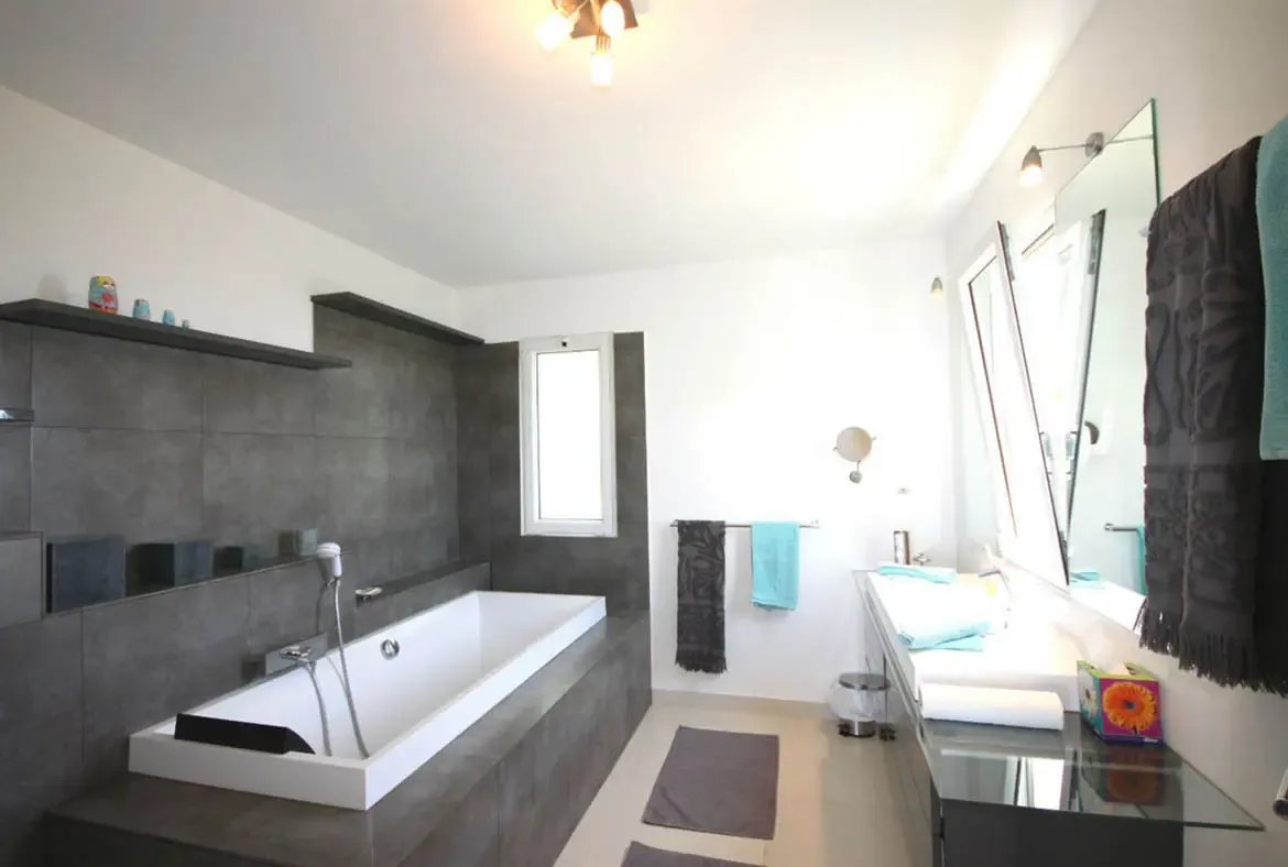 Indulge in a spa-like retreat within the contemporary ensuite, featuring a deep soaking tub and elegant dark tiling.