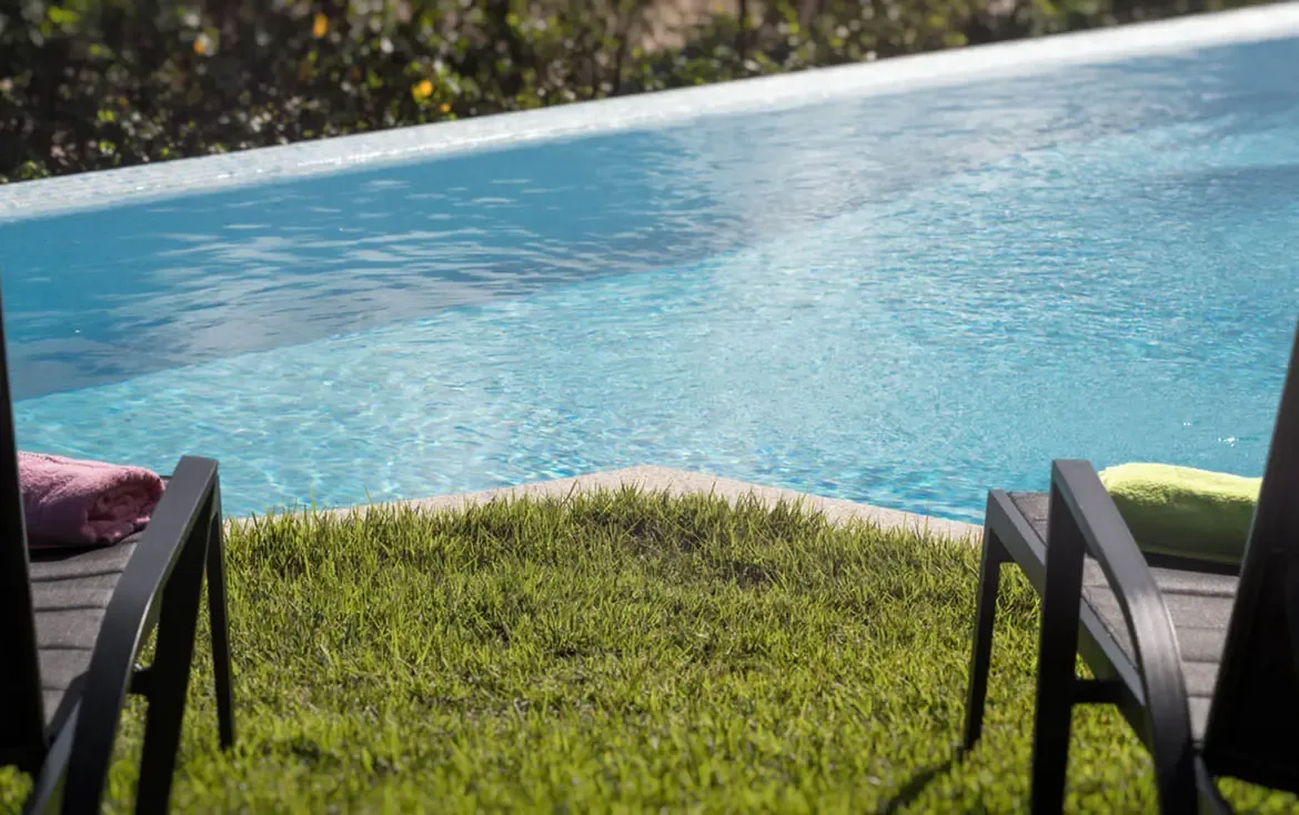 Pink and lime-green towels rest on modern loungers beside a bright blue infinity pool, where lush green foliage creates a private tropical backdrop.