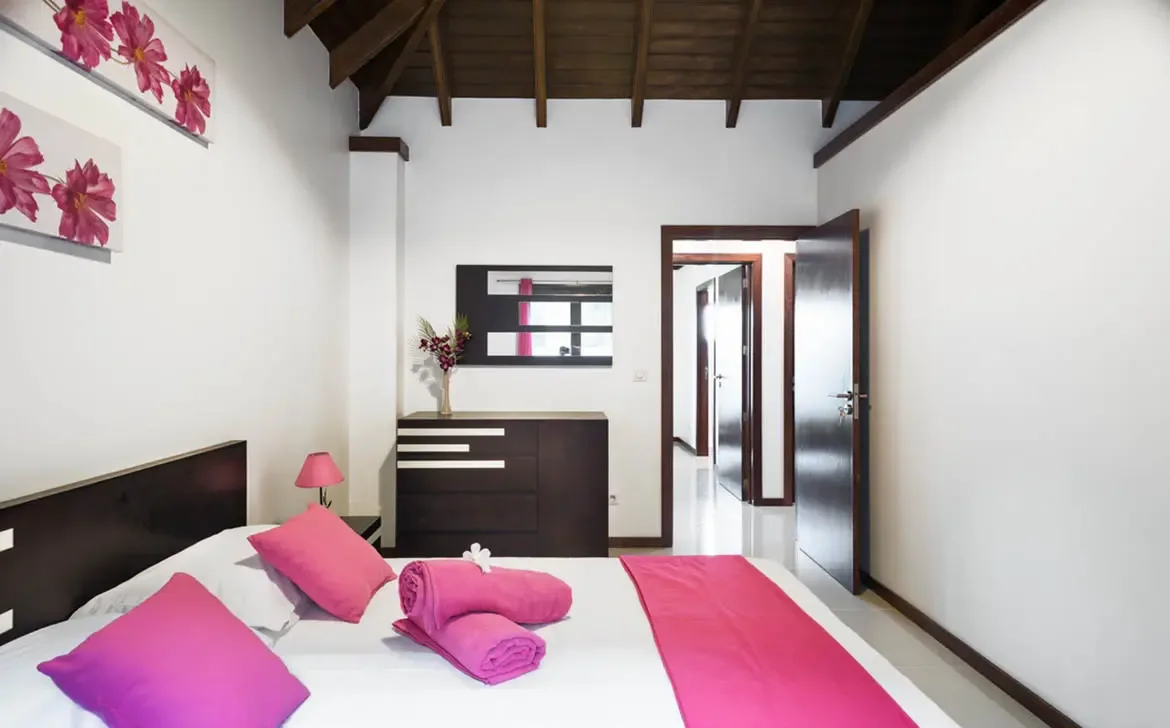 The villa's bedrooms combine traditional Caribbean charm with modern, vibrant decor, offering a serene and stylish retreat under vaulted wooden ceilings.