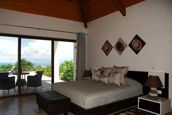 Wake up in this modern bedroom with high vaulted wood ceiling, large bed with decorative pillows, and sliding glass doors opening to a terrace with breathtaking ocean views.
